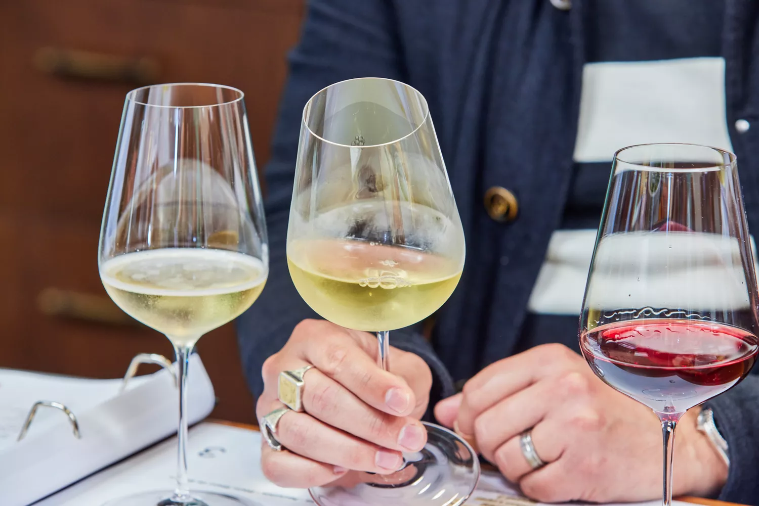 Person holding one of three Richard Brendon x Jancis Robinson The Perfect Wine Glass glasses filled with different wines in front of them