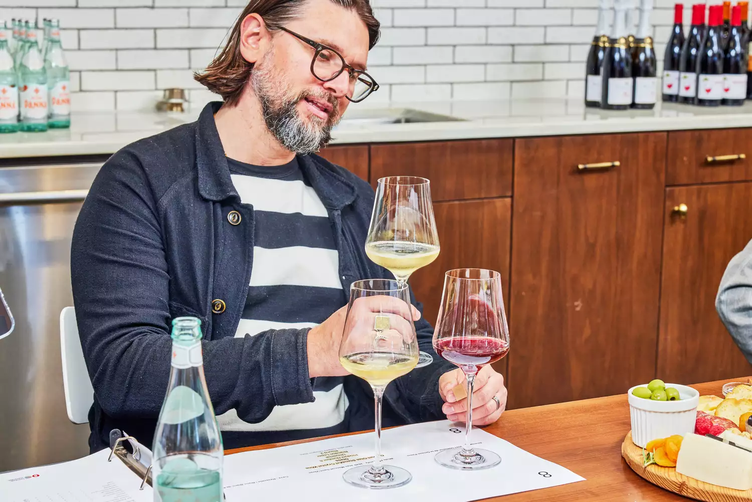 Person holding Gabriel-Glas StandArt Crystal Wine Glasses Set glass containing white wine with two more glasses on table